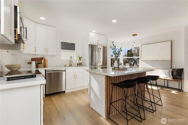 12852 Occidental Ave S, Seattle, WA 98168 - kitchen featuring stainless steel appliances, light wood-type flooring, a kitchen bar, backsplash, and recessed lighting