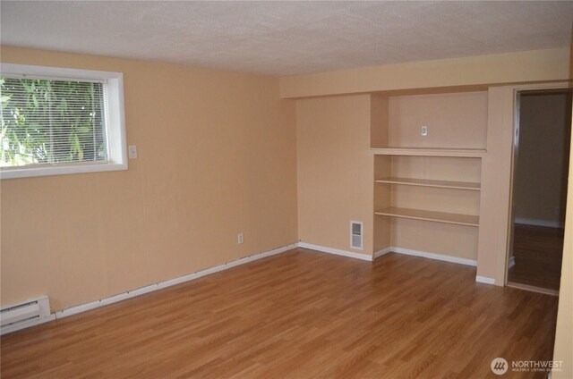 306 2nd St NE, Auburn, WA 98002 - unfurnished room featuring wood finished floors, a textured ceiling, built in features, and a baseboard heating unit