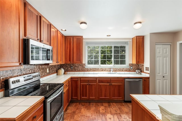4766 Mason St, Port Townsend, WA 98368 - kitchen featuring stainless steel appliances, tile counters, tasteful backsplash, light wood-type flooring, and brown cabinetry