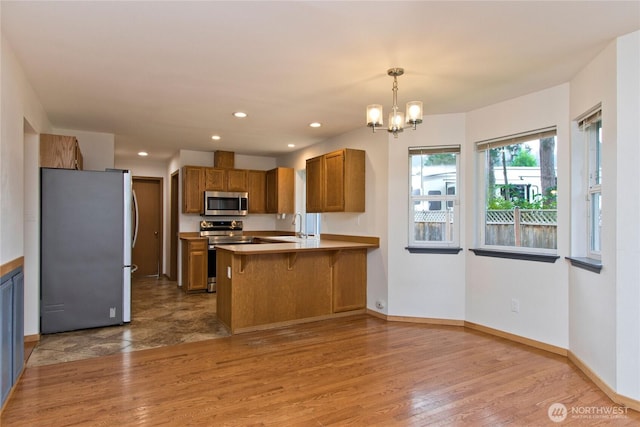 408 Cross Creek Ct, South Prairie, WA 98385 - kitchen with appliances with stainless steel finishes, brown cabinets, a peninsula, a chandelier, and wood finished floors