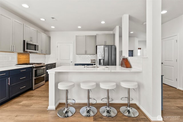 21552 SE 275th Ct, Maple Valley, WA 98038 - kitchen featuring appliances with stainless steel finishes, a breakfast bar area, a peninsula, light wood-style flooring, and decorative backsplash
