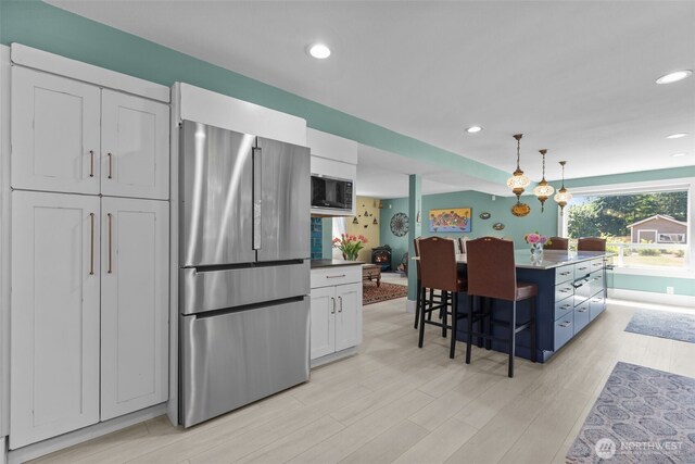 6830 SE Arlington Pl, Port Orchard, WA 98367 - kitchen featuring freestanding refrigerator, black microwave, a kitchen breakfast bar, pendant lighting, and recessed lighting