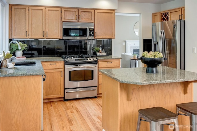 1125 Hemlock Ave SW, North Bend, WA 98045 - kitchen with appliances with stainless steel finishes, light wood-type flooring, decorative backsplash, light stone counters, and a breakfast bar area