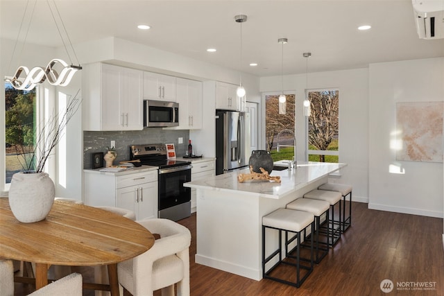 2749 Clare Ave Unit 1, Bremerton, WA 98310 - kitchen featuring appliances with stainless steel finishes, decorative backsplash, a center island with sink, dark wood-type flooring, and a breakfast bar area