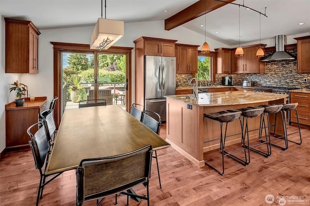 5829 112th Pl NE, Kirkland, WA 98033 - kitchen with freestanding refrigerator, wall chimney exhaust hood, an island with sink, decorative backsplash, and brown cabinetry