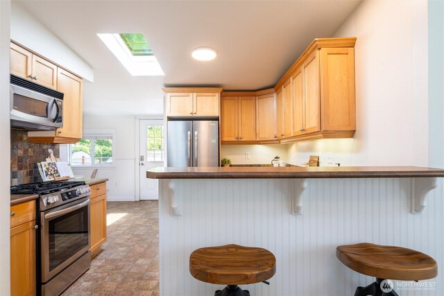 2226 King St, Bellingham, WA 98225 - kitchen featuring appliances with stainless steel finishes, a skylight, a kitchen breakfast bar, decorative backsplash, and light brown cabinetry