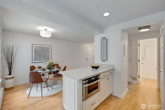 202 W Olympic Pl Unit 201, Seattle, WA 98119 - kitchen featuring oven, light wood-style floors, white cabinetry, light countertops, and a peninsula