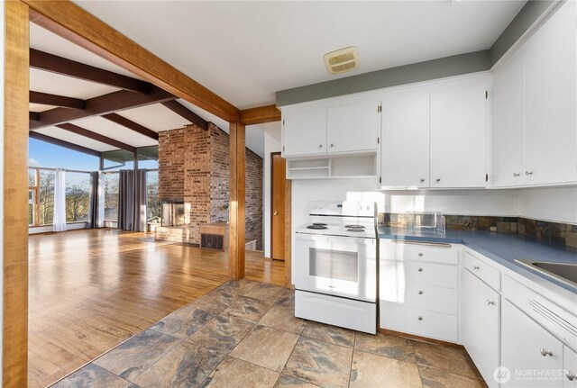 2104 E Ave, Anacortes, WA 98221 - kitchen with white range with electric cooktop, dark countertops, white cabinets, a multi sided fireplace, and brick wall