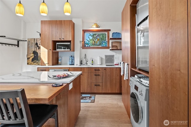 231 Benton, Leavenworth, WA 98826 - kitchen with washer / clothes dryer, stainless steel microwave, brown cabinetry, light wood finished floors, and hanging light fixtures
