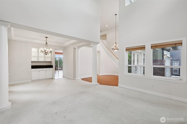 3301 Monterey Ct NE, Renton, WA 98056 - unfurnished living room featuring a chandelier, light colored carpet, a towering ceiling, ornate columns, and a tray ceiling