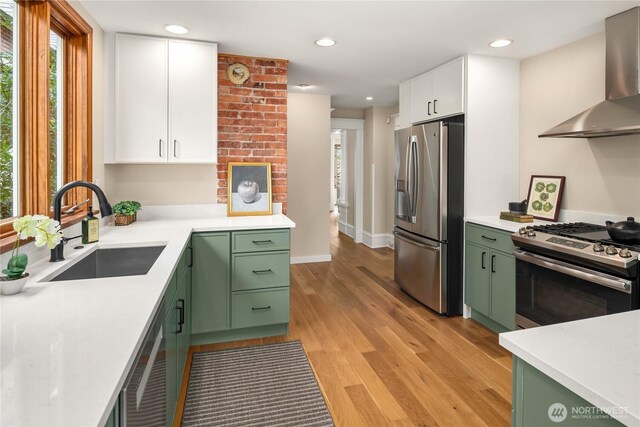2401 10th Ave W, Seattle, WA 98119 - kitchen with green cabinetry, stainless steel appliances, wall chimney range hood, white cabinets, and light wood-style flooring