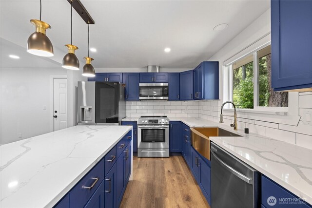 5206 68th Ave W, University Place, WA 98467 - kitchen featuring appliances with stainless steel finishes, decorative backsplash, blue cabinetry, light wood-style floors, and light stone counters
