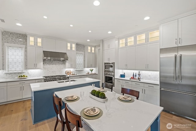 3348 218th St SE, Bothell, WA 98021 - kitchen featuring built in appliances, exhaust hood, a kitchen island with sink, decorative backsplash, and light countertops