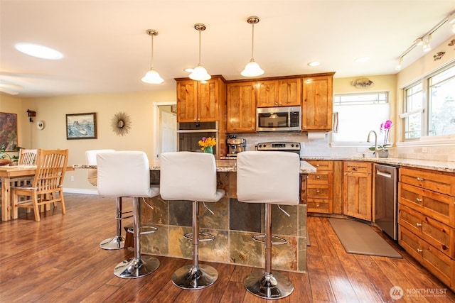 516 E Willow St, Sequim, WA 98382 - kitchen featuring stainless steel appliances, a kitchen breakfast bar, brown cabinetry, dark wood finished floors, and recessed lighting