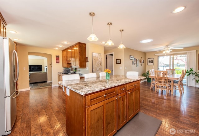 516 E Willow St, Sequim, WA 98382 - kitchen featuring freestanding refrigerator, arched walkways, a ceiling fan, dark wood-style flooring, and light stone countertops