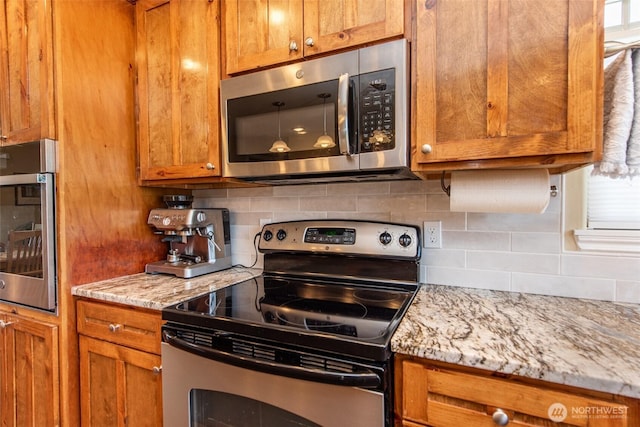 516 E Willow St, Sequim, WA 98382 - kitchen featuring stainless steel appliances, brown cabinets, decorative backsplash, and light stone counters