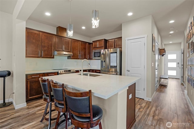 2015 79th St SE, Everett, WA 98203 - kitchen featuring appliances with stainless steel finishes, under cabinet range hood, dark wood-type flooring, pendant lighting, and a center island with sink