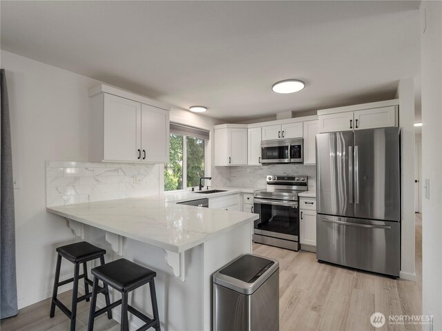 17301 6th Ave E, Spanaway, WA 98387 - kitchen with appliances with stainless steel finishes, a peninsula, light wood-style floors, white cabinets, and tasteful backsplash