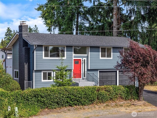 17301 6th Ave E, Spanaway, WA 98387 - split foyer home with a chimney, an attached garage, a shingled roof, and driveway