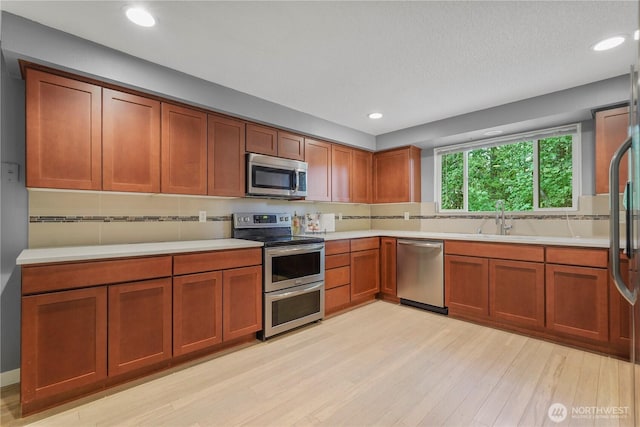 13719 Pinehurst Ln NW, Gig Harbor, WA 98329 - kitchen featuring appliances with stainless steel finishes, light countertops, light wood-style floors, recessed lighting, and brown cabinets