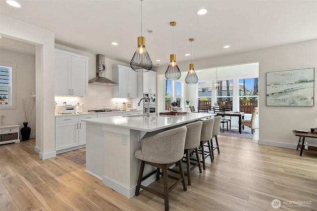 18740 130th St E, Bonney Lake, WA 98391 - kitchen with wall chimney exhaust hood, gas cooktop, recessed lighting, light wood-style floors, and a breakfast bar