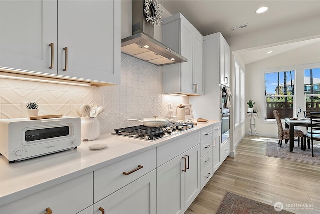 18740 130th St E, Bonney Lake, WA 98391 - kitchen with wall chimney exhaust hood, stainless steel gas cooktop, light countertops, light wood finished floors, and decorative backsplash