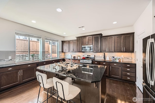 3613 198th Pl SE, Bothell, WA 98012 - kitchen featuring appliances with stainless steel finishes, dark wood-type flooring, dark brown cabinets, dark stone countertops, and a breakfast bar