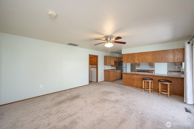 206 E St NE, Ephrata, WA 98823 - kitchen featuring brown cabinetry, light carpet, ceiling fan, a peninsula, and a kitchen bar