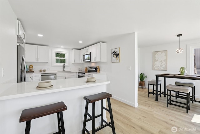 12448 Occidental Ave S, Seattle, WA 98168 - kitchen with appliances with stainless steel finishes, a peninsula, a kitchen breakfast bar, light wood-style floors, and white cabinets