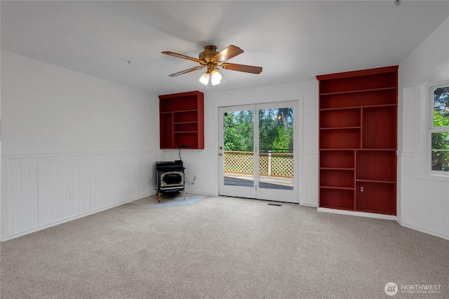 19517 Whiteman Cove Rd SW, Longbranch, WA 98351 - unfurnished living room with a wood stove, a ceiling fan, carpet floors, and a wainscoted wall