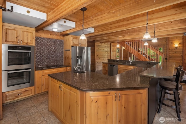 7717 252nd Ave NE, Redmond, WA 98053 - kitchen with stainless steel appliances, a wooden ceiling with exposed beams, a large island, wooden walls, and light brown cabinets