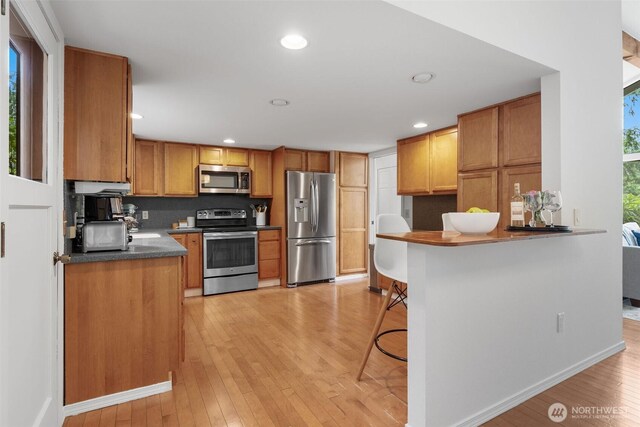 14913 SE 47th Ct, Bellevue, WA 98006 - kitchen featuring stainless steel appliances, light wood-type flooring, dark countertops, a peninsula, and recessed lighting