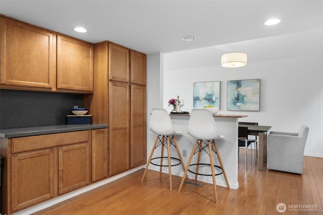 14913 SE 47th Ct, Bellevue, WA 98006 - kitchen with brown cabinets, light wood-style flooring, a breakfast bar, dark countertops, and recessed lighting