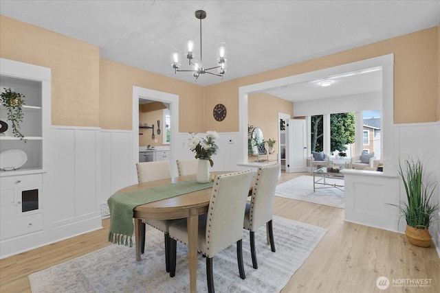 3443 21st Ave W, Seattle, WA 98199 - dining room featuring a chandelier, light wood finished floors, a wainscoted wall, and a decorative wall