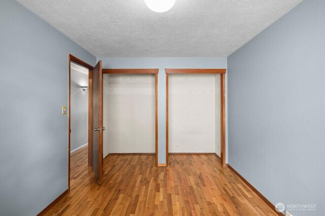 5142 N 27th St, Tacoma, WA 98407 - unfurnished bedroom with a textured ceiling, light wood-type flooring, and multiple closets