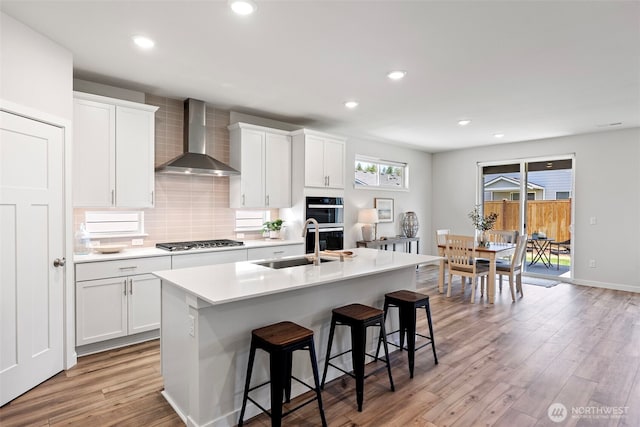 18231 132nd Ave E, Puyallup, WA 98374 - kitchen with wall chimney range hood, stainless steel gas stovetop, a center island with sink, light wood-style flooring, and backsplash