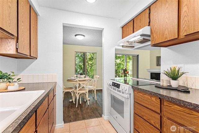 3100 Bill Mcdonald Pkwy Unit E101, Bellingham, WA 98225 - kitchen with electric range, under cabinet range hood, brown cabinets, light tile patterned floors, and a fireplace