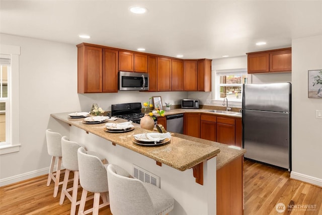 5235 11th Ave NE Unit A, Seattle, WA 98105 - kitchen featuring stainless steel appliances, brown cabinetry, a peninsula, a kitchen bar, and recessed lighting