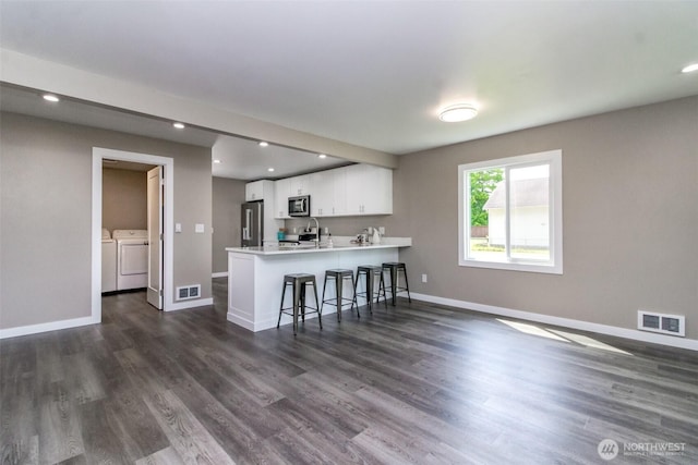 318 Mill Ave SE, Orting, WA 98360 - kitchen featuring appliances with stainless steel finishes, independent washer and dryer, a peninsula, white cabinetry, and a kitchen breakfast bar
