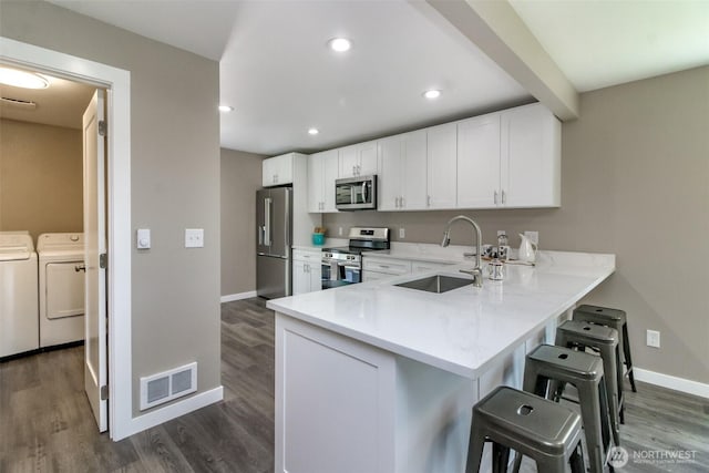 318 Mill Ave SE, Orting, WA 98360 - kitchen featuring stainless steel appliances, washer and dryer, dark wood-type flooring, a breakfast bar, and recessed lighting