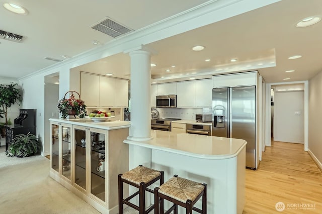 9727 NE Juanita Dr Unit 201, Kirkland, WA 98034 - kitchen featuring stainless steel appliances, a peninsula, a kitchen breakfast bar, ornate columns, and light countertops