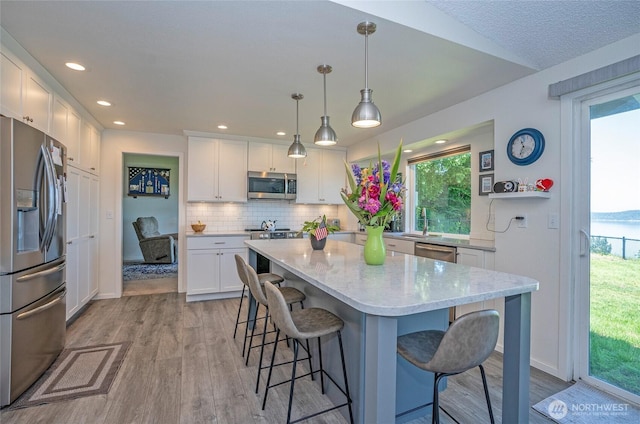 96 Kim Ct, Steilacoom, WA 98388 - kitchen featuring appliances with stainless steel finishes, light wood-type flooring, white cabinets, a kitchen bar, and plenty of natural light