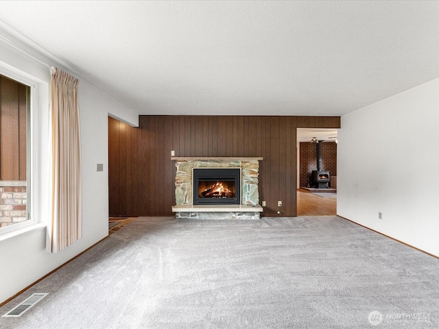 6702 120th St E, Puyallup, WA 98373 - unfurnished living room with carpet floors, a wood stove, wood walls, and a stone fireplace