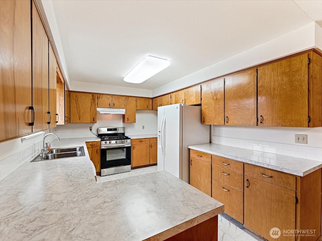 6702 120th St E, Puyallup, WA 98373 - kitchen featuring stainless steel gas stove, white fridge with ice dispenser, under cabinet range hood, brown cabinetry, and light countertops