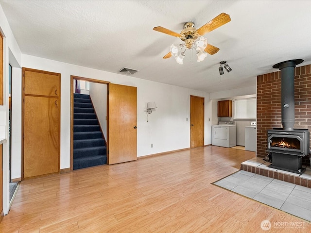 6702 120th St E, Puyallup, WA 98373 - unfurnished living room with washer and clothes dryer, a wood stove, light wood-style flooring, a ceiling fan, and stairs