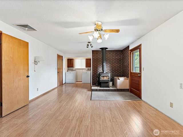 6702 120th St E, Puyallup, WA 98373 - unfurnished living room with washing machine and clothes dryer, light wood-style floors, a wood stove, ceiling fan, and a textured ceiling