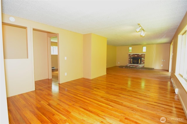 3428 99th Ave NE, Lake Stevens, WA 98258 - unfurnished living room with light wood finished floors, a textured ceiling, a fireplace, and a baseboard heating unit