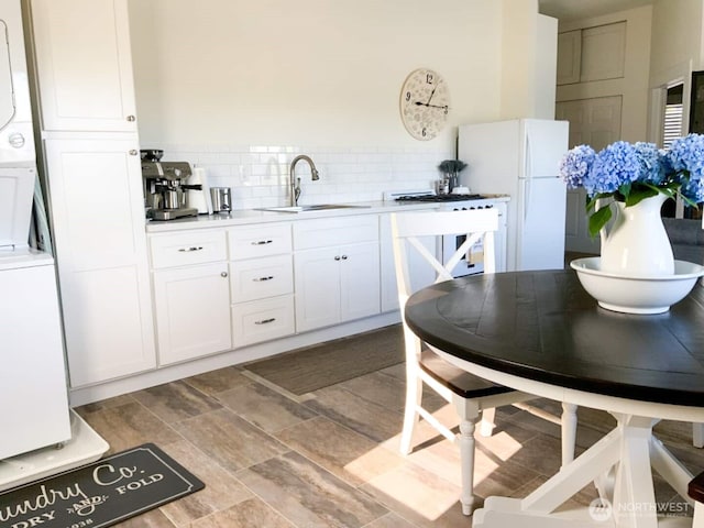 614 16th St SW, Puyallup, WA 98371 - kitchen featuring stacked washer and clothes dryer, freestanding refrigerator, white cabinets, light countertops, and tasteful backsplash