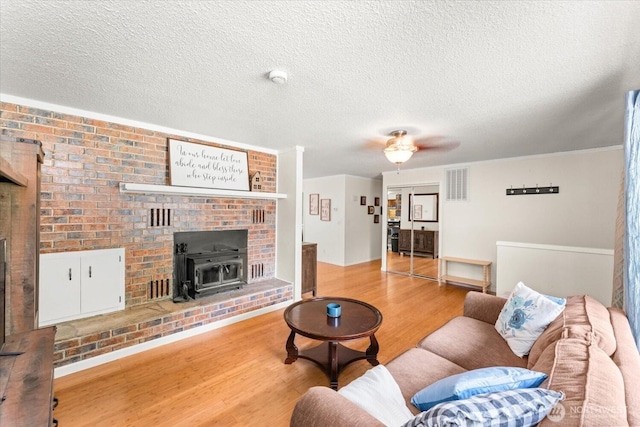 707 Kenwood St N, Omak, WA 98841 - living room with a wood stove, light wood-style floors, a textured ceiling, and a ceiling fan