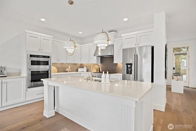 424 3rd Ln S Unit 12, Kirkland, WA 98033 - kitchen featuring stainless steel appliances, wall chimney range hood, light wood-style flooring, tasteful backsplash, and decorative light fixtures